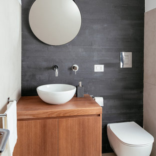 Foto di un piccolo bagno di servizio contemporaneo con ante lisce, ante in legno scuro, WC sospeso, piastrelle nere, piastrelle in ardesia, pavimento in gres porcellanato, lavabo a bacinella, top in legno, pareti nere e pavimento grigio