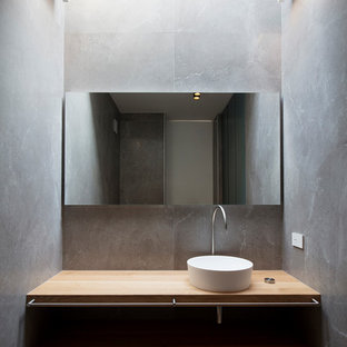 Immagine di un bagno di servizio minimalista di medie dimensioni con nessun'anta, ante in legno chiaro, piastrelle grigie, pareti grigie, lavabo a bacinella e top in legno