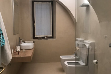 Cette image montre un grand WC et toilettes design en bois clair avec WC séparés, un carrelage beige, un mur beige, une vasque, un plan de toilette en bois, meuble-lavabo suspendu et un plafond voûté.