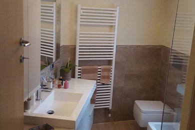 Immagine di un piccolo bagno di servizio moderno con WC sospeso, piastrelle beige, piastrelle in ceramica, pareti beige, pavimento in laminato, lavabo integrato, pavimento beige e top bianco