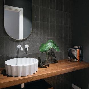 Esempio di un bagno di servizio contemporaneo di medie dimensioni con nessun'anta, ante in legno scuro, piastrelle nere, pareti nere, lavabo a bacinella, top in legno, pavimento marrone, top marrone e mobile bagno sospeso
