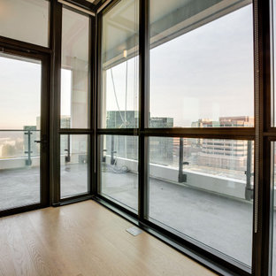 Cette image montre un très grand balcon minimaliste d'appartement avec une extension de toiture et un garde-corps en verre.