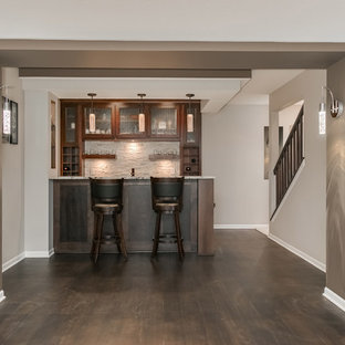 Exemple d'un grand sous-sol chic donnant sur l'extérieur avec un mur gris, un sol en bois foncé, une cheminée d'angle, un manteau de cheminée en carrelage et un sol marron.
