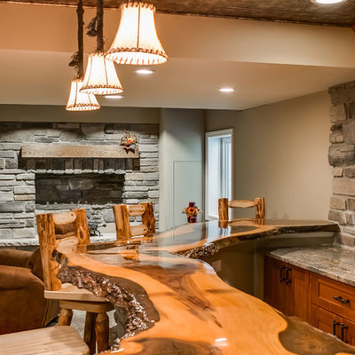 Example of a large mountain style look-out medium tone wood floor and beige floor basement design in Chicago with gray walls, a standard fireplace and a stone fireplace
