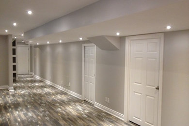 Modelo de sótano con puerta moderno de tamaño medio sin chimenea con paredes beige y suelo de madera en tonos medios