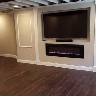 Idée de décoration pour un sous-sol tradition semi-enterré et de taille moyenne avec un mur beige, un sol en bois foncé, une cheminée ribbon, un manteau de cheminée en plâtre et un sol marron.