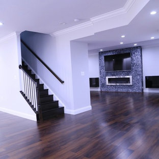 Réalisation d'un grand sous-sol design donnant sur l'extérieur avec un mur gris, sol en stratifié, une cheminée standard, un manteau de cheminée en carrelage et un sol marron.