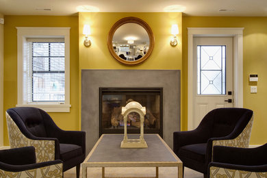 カルガリーにある高級な中くらいなトランジショナルスタイルのおしゃれな地下室 (半地下 (窓あり) 、黄色い壁、磁器タイルの床、標準型暖炉、コンクリートの暖炉まわり、ベージュの床) の写真