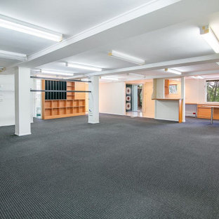 Exemple d'un grand sous-sol tendance donnant sur l'extérieur avec salle de jeu, un mur blanc, moquette, un sol noir et un plafond en poutres apparentes.
