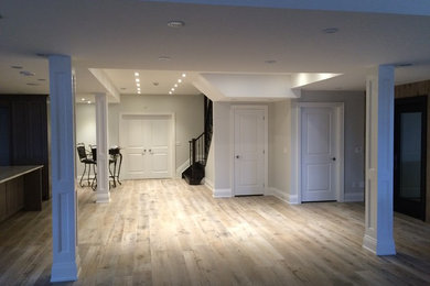 トロントにある高級な広いトランジショナルスタイルのおしゃれな地下室 (全地下、グレーの壁、淡色無垢フローリング、暖炉なし、ベージュの床) の写真