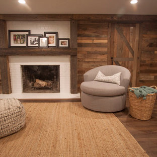 Cette image montre un grand sous-sol chalet semi-enterré avec un mur marron, un sol en bois brun, une cheminée standard, un manteau de cheminée en brique et un sol marron.
