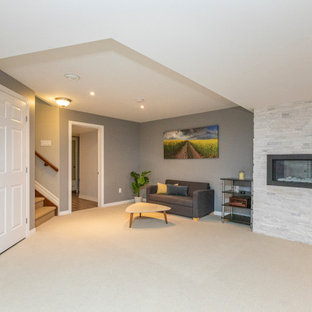 Idée de décoration pour un grand sous-sol design avec un mur gris, moquette, une cheminée standard, un manteau de cheminée en pierre de parement et un sol beige.