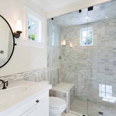 Island style 3/4 gray tile gray floor alcove shower photo in Miami with shaker cabinets, white cabinets, beige walls, a drop-in sink, a hinged shower door, white countertops, a one-piece toilet and marble countertops