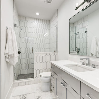 Alcove shower - large transitional 3/4 white tile and porcelain tile porcelain tile and gray floor alcove shower idea in Dallas with shaker cabinets, gray cabinets, a two-piece toilet, white walls, an undermount sink, a hinged shower door, white countertops and a built-in vanity