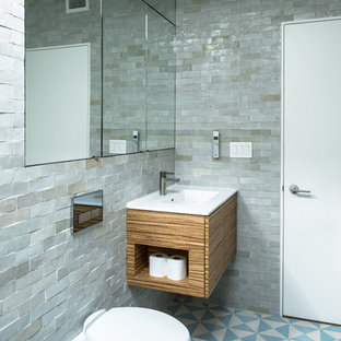 This is an example of a mid-sized industrial master bathroom in New York with flat-panel cabinets, medium wood cabinets, a wall-mount toilet, gray tile, a drop-in tub, an open shower, stone tile, grey walls, ceramic floors, a drop-in sink, solid surface benchtops and blue floor.