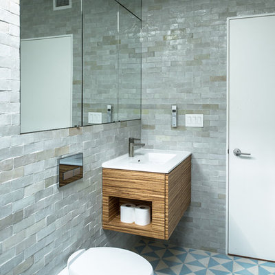 Bathroom - mid-sized industrial master gray tile and stone tile ceramic tile and blue floor bathroom idea in New York with flat-panel cabinets, medium tone wood cabinets, a wall-mount toilet, gray walls, a drop-in sink and solid surface countertops