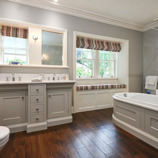 Classic ensuite bathroom in Other with shaker cabinets, grey cabinets, a built-in bath, a corner shower, white tiles, grey walls, a submerged sink, brown floors and a hinged door.
