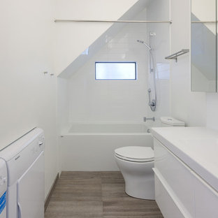 Cette image montre une salle d'eau design avec un placard à porte plane, des portes de placard blanches, une baignoire en alcôve, un combiné douche/baignoire, un carrelage blanc, un lavabo intégré, un plan de toilette en quartz modifié, des carreaux de céramique, un mur blanc, un sol en carrelage de céramique et buanderie.