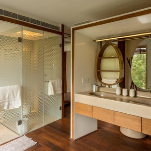 Inspiration for an asian master bathroom in Pune with flat-panel cabinets, medium wood cabinets, an alcove shower, beige tile, beige walls, dark hardwood floors, an integrated sink, brown floor, a hinged shower door and beige benchtops.