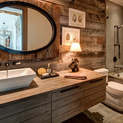 Example of a mid-sized mountain style 3/4 gray tile tub/shower combo design in Salt Lake City with medium tone wood cabinets, brown walls, a vessel sink, an undermount tub, a one-piece toilet, wood countertops and brown countertops
