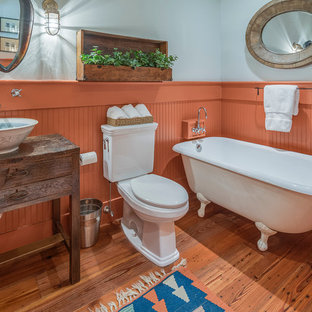 Inspiration for a farmhouse medium tone wood floor claw-foot bathtub remodel in Atlanta with a vessel sink, furniture-like cabinets, dark wood cabinets, a two-piece toilet and orange walls