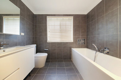 シドニーにある広いコンテンポラリースタイルのおしゃれなマスターバスルーム (置き型浴槽、分離型トイレ、フラットパネル扉のキャビネット、白いキャビネット、コーナー設置型シャワー、茶色いタイル、セメントタイル、茶色い壁、一体型シンク、茶色い床、開き戸のシャワー) の写真