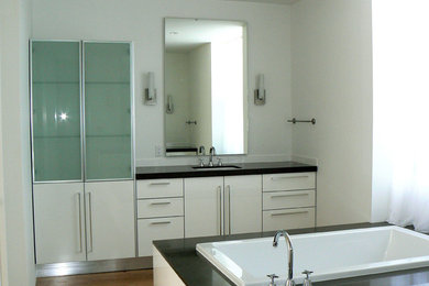 Kleines Modernes Badezimmer En Suite mit flächenbündigen Schrankfronten, weißen Schränken, freistehender Badewanne, weißer Wandfarbe, braunem Holzboden, Unterbauwaschbecken, Laminat-Waschtisch und braunem Boden in San Diego