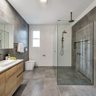 This is an example of a mid-sized contemporary 3/4 bathroom in Brisbane with flat-panel cabinets, beige cabinets, a corner shower, a wall-mount toilet, gray tile, porcelain tile, white walls, porcelain floors, a vessel sink, grey floor, a hinged shower door and white benchtops.