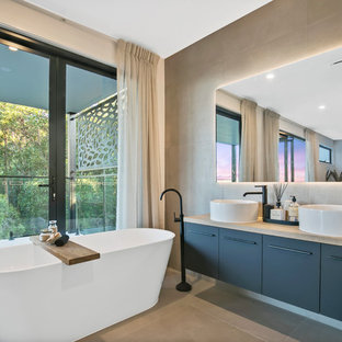 Photo of a contemporary master bathroom in Sunshine Coast with flat-panel cabinets, grey cabinets, a freestanding tub, gray tile, white walls, a vessel sink, wood benchtops, grey floor and beige benchtops.