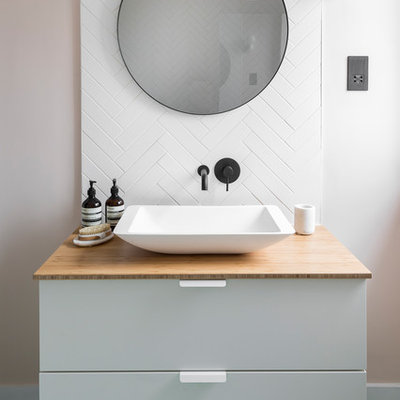 Danish white tile green floor bathroom photo in London with flat-panel cabinets, white cabinets, white walls, a vessel sink, wood countertops and beige countertops