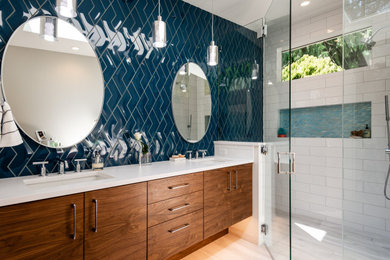 Medium sized modern ensuite bathroom in Seattle with flat-panel cabinets, brown cabinets, a built-in shower, a two-piece toilet, blue tiles, porcelain tiles, white walls, porcelain flooring, a submerged sink, engineered stone worktops, grey floors, a hinged door, white worktops, a wall niche, double sinks, a built in vanity unit and wainscoting.
