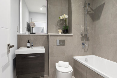 Cette image montre une salle de bain minimaliste avec une baignoire en alcôve, un combiné douche/baignoire, WC à poser, un carrelage gris, un lavabo intégré et un plan de toilette blanc.