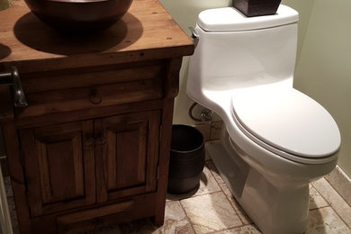 Small mountain style multicolored tile and stone tile travertine floor bathroom photo in Kansas City with a vessel sink, furniture-like cabinets, distressed cabinets, wood countertops and a one-piece toilet