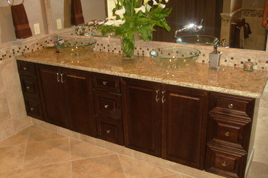 Example of a trendy beige tile and stone tile freestanding bathtub design in Portland with a vessel sink, a one-piece toilet, raised-panel cabinets, dark wood cabinets and granite countertops