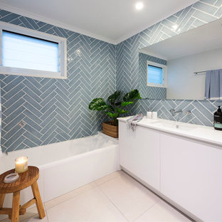 Design ideas for a mid-sized beach style 3/4 bathroom in Sunshine Coast with white cabinets, blue tile, ceramic tile, ceramic floors, an undermount sink, engineered quartz benchtops, beige floor, white benchtops, flat-panel cabinets, an alcove tub and blue walls.