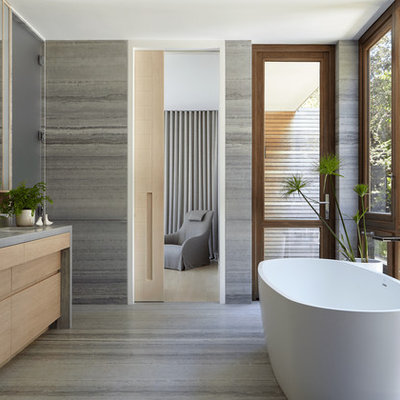 Example of a beach style master gray tile gray floor freestanding bathtub design in New York with gray countertops, flat-panel cabinets, light wood cabinets, gray walls and an undermount sink