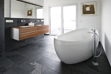Large modern ensuite bathroom in Chicago with black tiles, ceramic tiles, flat-panel cabinets, medium wood cabinets, a freestanding bath, white walls, slate flooring, a submerged sink and wooden worktops.