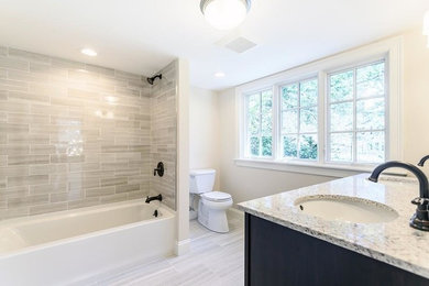Example of a mid-sized classic 3/4 gray tile and ceramic tile cement tile floor and gray floor drop-in bathtub design in Boston with shaker cabinets, brown cabinets, a two-piece toilet, beige walls, an undermount sink, quartzite countertops and white countertops