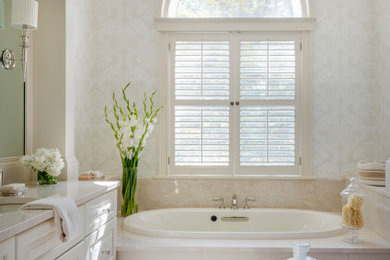 Drop-in bathtub - traditional beige tile and stone slab beige floor and wallpaper drop-in bathtub idea in Boston with raised-panel cabinets, white cabinets, beige walls, an undermount sink, white countertops and a built-in vanity