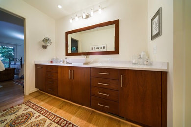 Diseño de cuarto de baño principal moderno grande con lavabo sobreencimera, armarios con paneles lisos, puertas de armario de madera oscura, paredes blancas, suelo de madera clara y encimera de mármol