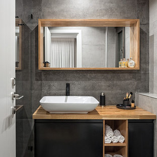 Bild på ett litet minimalistiskt brun brunt badrum med dusch, med laminatgolv, släta luckor, svarta skåp, grå kakel, grå väggar, ett fristående handfat, träbänkskiva och grått golv