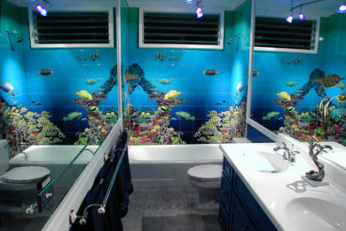 ハワイにあるトロピカルスタイルのおしゃれな浴室 (青いキャビネット、コーナー型浴槽、一体型トイレ	、黒いタイル、セメントタイル、青い壁、オーバーカウンターシンク、黒い床、白い洗面カウンター) の写真
