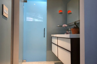 Design ideas for a medium sized contemporary ensuite bathroom in New York with glass-front cabinets, medium wood cabinets, an alcove shower, blue walls, marble flooring, a wall-mounted sink and white worktops.