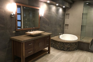 Large trendy master gray tile and stone tile porcelain tile and beige floor bathroom photo in Chicago with flat-panel cabinets, medium tone wood cabinets, multicolored walls, a vessel sink, limestone countertops and a hinged shower door