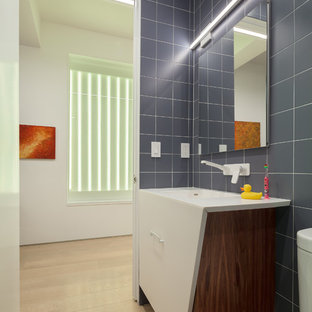 Example of a small trendy kids' blue tile and ceramic tile light wood floor and beige floor alcove shower design in New York with furniture-like cabinets, a two-piece toilet, blue walls, an integrated sink, solid surface countertops and a hinged shower door