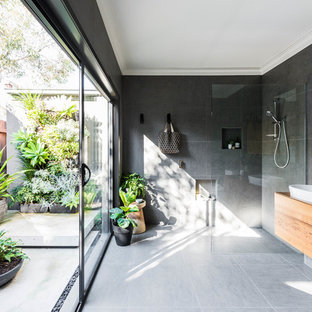 This is an example of a large contemporary master bathroom in Melbourne with flat-panel cabinets, brown cabinets, a curbless shower, gray tile, grey walls, a vessel sink, wood benchtops, grey floor, an open shower and brown benchtops.