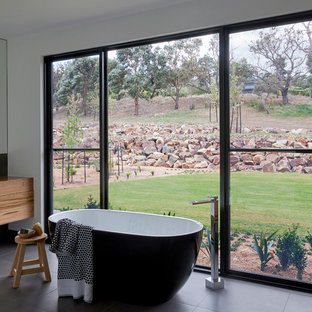 Contemporary bathroom in Other with flat-panel cabinets, medium wood cabinets, a freestanding tub, white walls, wood benchtops, black floor and brown benchtops.