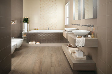 Drop-in bathtub - large contemporary master beige tile and porcelain tile light wood floor and beige floor drop-in bathtub idea in Denver with a vessel sink, flat-panel cabinets, solid surface countertops, a wall-mount toilet, beige walls and light wood cabinets