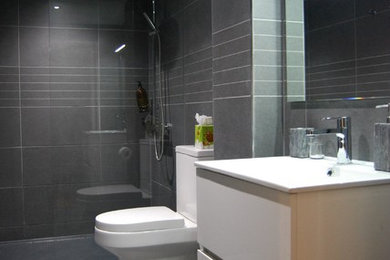 Immagine di una grande stanza da bagno con doccia minimalista con ante lisce, ante bianche, doccia aperta, WC monopezzo, piastrelle grigie, piastrelle in pietra, pareti grigie, pavimento con piastrelle in ceramica e lavabo integrato