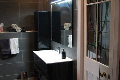 Cette image montre une grande salle d'eau minimaliste avec un placard en trompe-l'oeil, des portes de placard noires, une douche ouverte, WC suspendus, un carrelage gris, des carreaux de céramique, un sol en carrelage de céramique et un lavabo intégré.